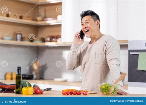 Positive Chinese Man Cooking Healthy Salad And Talking On Phone Stock