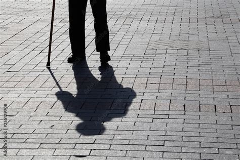 Silhouette Of Man Walking With A Cane Long Shadow On Pavement Concept