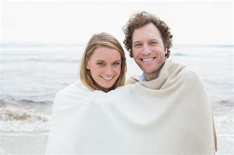 premium photo smiling couple wrapped in blanket at beach