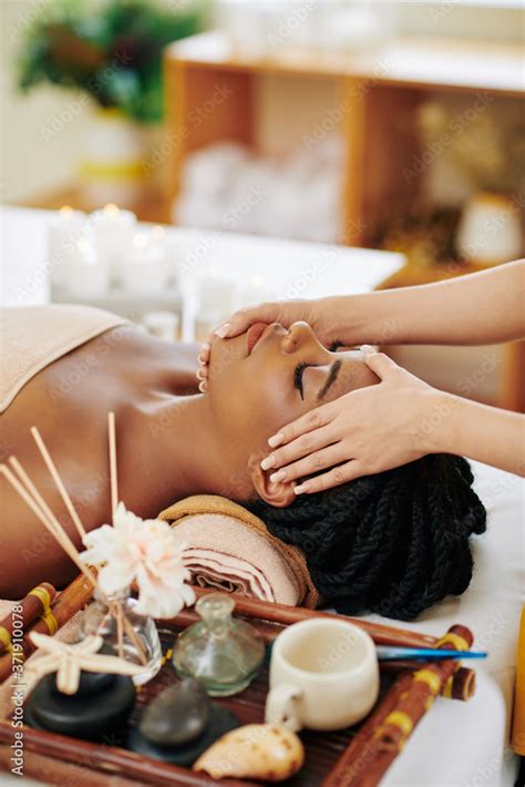 Beautiful Young Black Woman Enjoying Face And Head Massage In Spa Salon When Lying On Bed Next