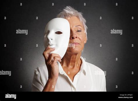 serious looking older woman revealing true face behind mask Stock Photo