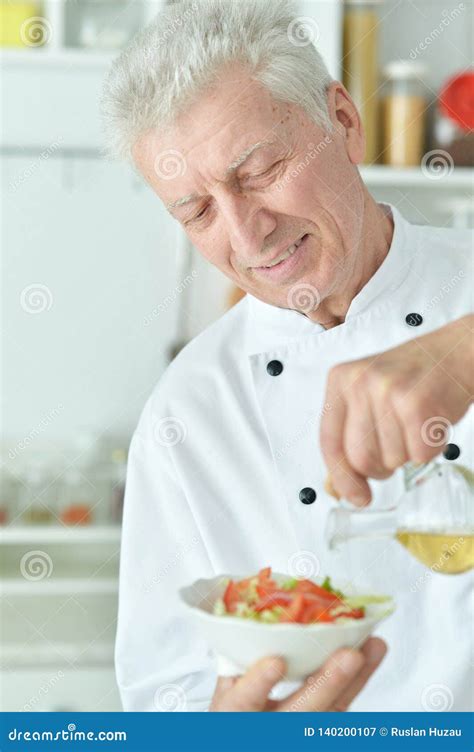 Portrait Of Elderly Male Chef Pouring Oil Into Salad Stock Image