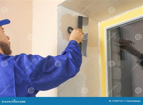 Professional Worker Plastering Window Area With Putty Knife Indoors