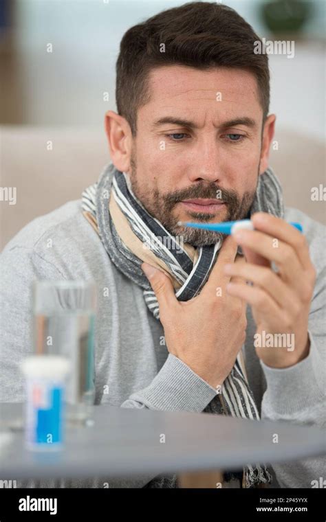 Sick Man Lying On Sofa Checking His Temperature At Home Stock Photo Alamy