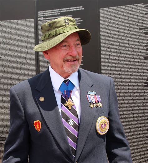 An Older Man In A Suit And Tie Standing Next To A Wall With Medals On It
