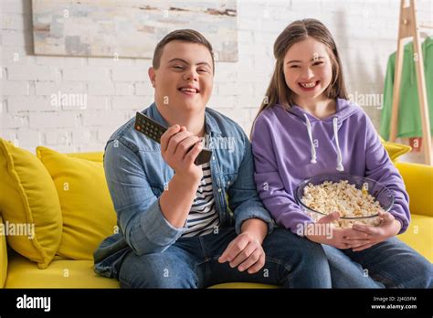 glückliche teenager mit down syndrom die fernbedienung und popcorn auf der couch hielten