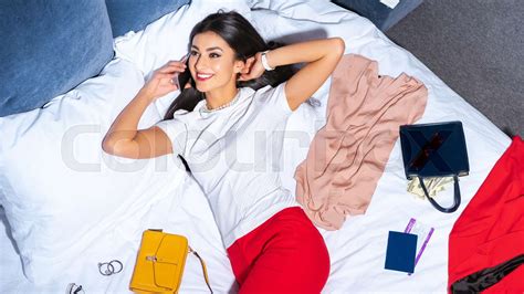 Beautiful Smiling Woman Talking By Smartphone While Lying On Bed With Stylish Clothes Passport