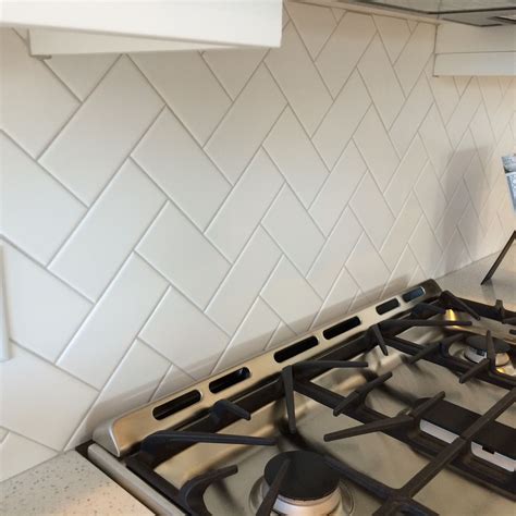 3x6 white subway tile in a herringbone pattern with light gray grout finishes floors walls