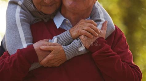 Aged Caucasian Woman Hugs Her Husband From The Back Holding Hands