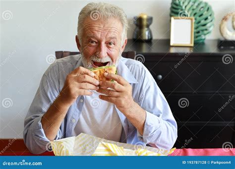 Feliz Caucásico Anciano Comiendo Hamburguesa En La Sala De Estar Con