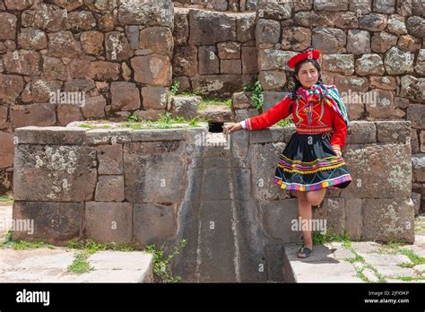 Peruvian Indigenous Quechua Woman By A Inca Wall With Fountain In The