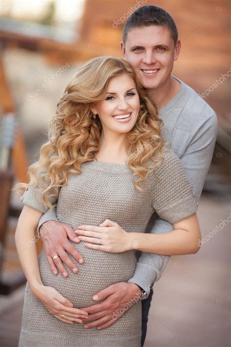 Young Pregnant Woman With Husband Walking Outdoor And Hugs Tummy