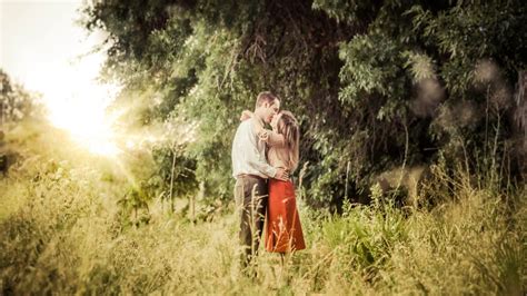 Photography Of Man And Woman Kissing While Standing On Grass While Facing Sunlight Hd Wallpaper
