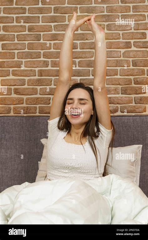 Beautiful Woman Sits On The Bed Stretches Her Arms Up After Sleeping
