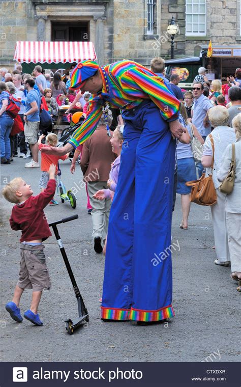 A Man Dressed As A Clown Walks On Stilts And Gives High Five To Young