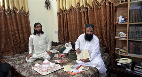 leader of the lashkar e jhangvi ishaq sits on a bed with his son malik usman as he shows a book