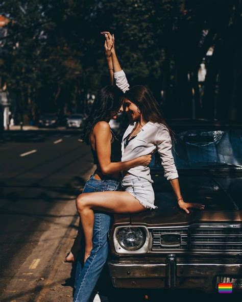 Two Women Are Sitting On The Hood Of A Car And One Is Holding Her Leg Up