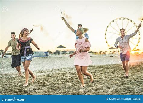 Group Of Happy Friends Running On The Beach With Fireworks Sparklers