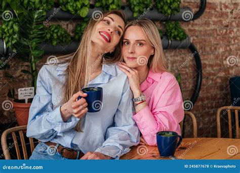 Two Women Friends Sitting In Cafe Drinking Coffee And Hugging Smiling Caucasian Girls Chatting