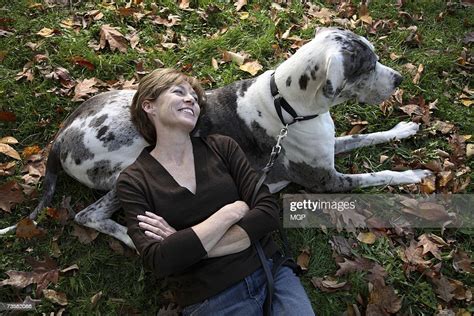 Mature Woman Lying On Great Dane In Park Smiling High Res Stock Photo