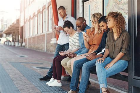 Passing The Time As They Wait A Group Of People Using Their Cellphones While Sitting At A Bus