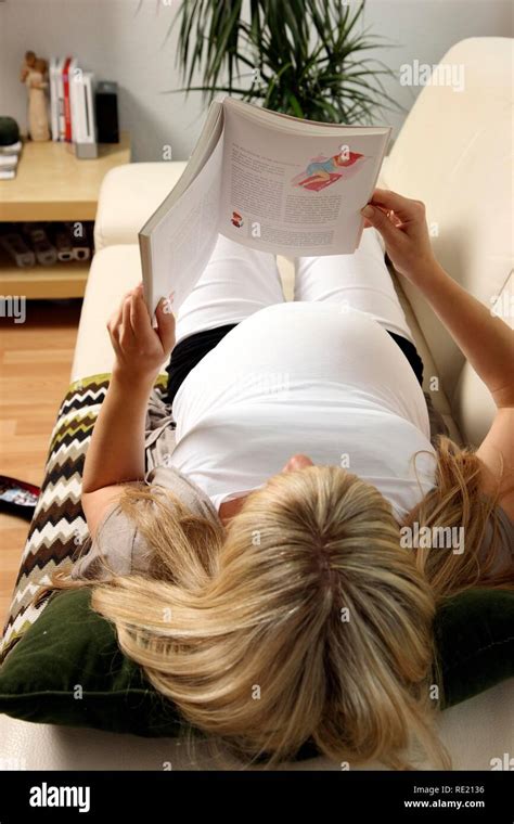 Pregnant Woman 9th Month Lying On The Sofa At Home And Reading A Book About Pregnancy Stock