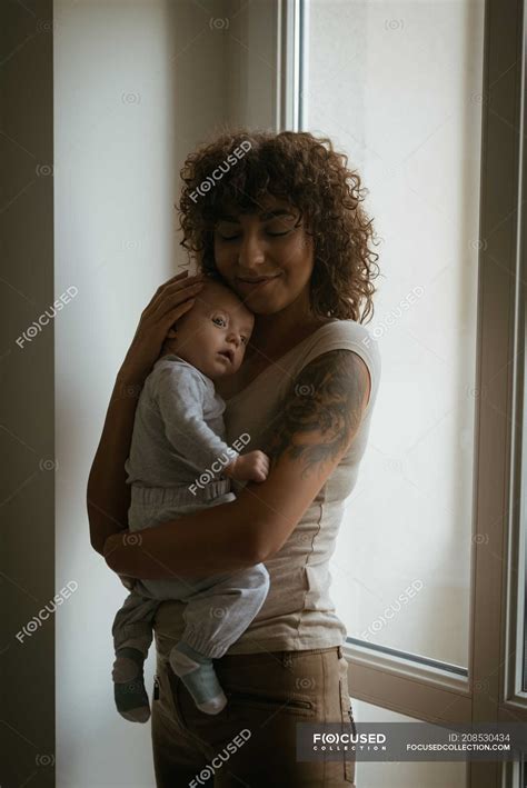 Affectionate Mother Embracing Her Baby At Home Baby Clothing