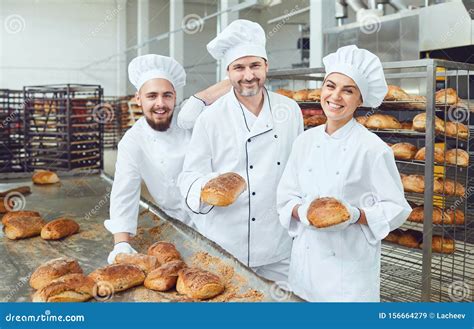 Bakers Smiling Holding Fresh Bread In Their Hands In A Bakery Stock