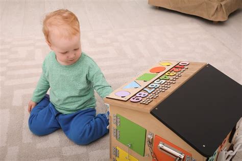 Cute Little Boy Playing With Busy Board House On Floor Stock Photo