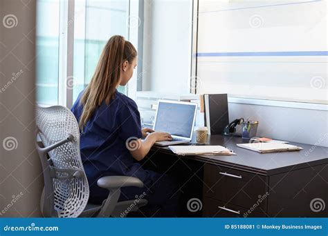 Nurse Wearing Scrubs Working At Desk In Office Stock Image Image Of