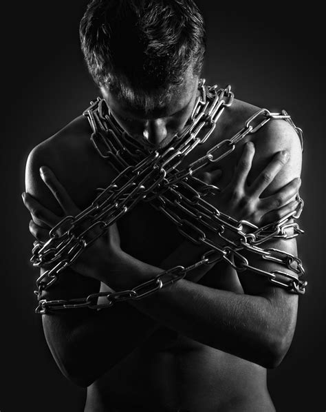 A Man Wrapped In Chains With His Hands On His Chest Looking Down At The Camera