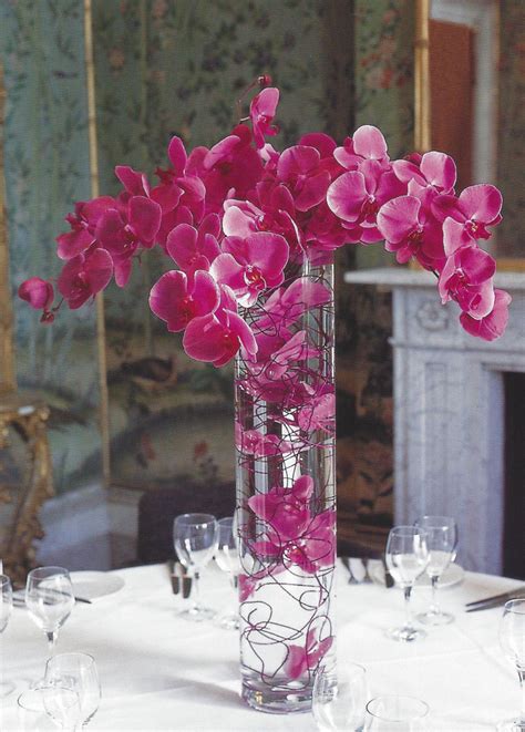 A Tall Vase Filled With Pink Flowers On Top Of A White Table Cloth