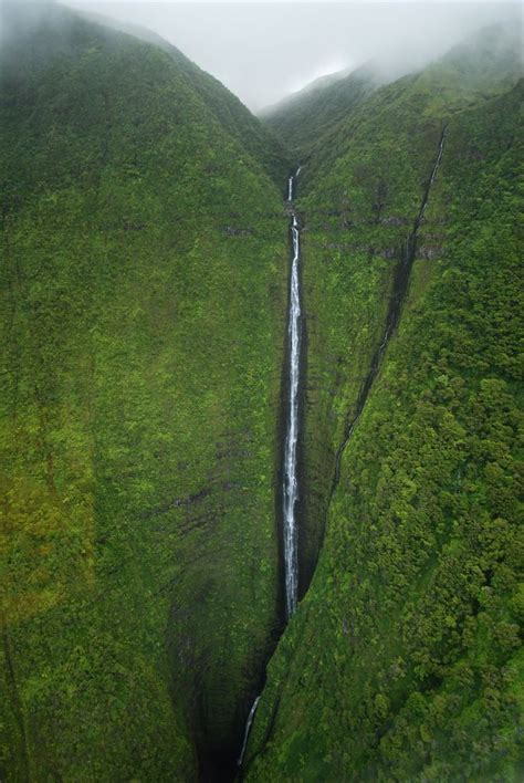 An Aerial View Of A Waterfall In The Middle Of A Green Mountain With