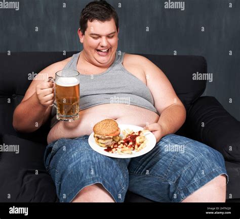 Something To Wash Down His Meal An Obese Young Man Sitting On A Sofa