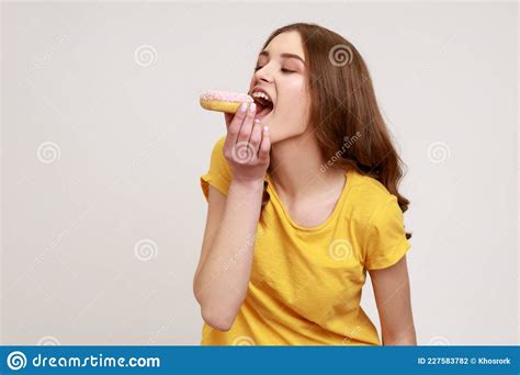 Hungry Girl With Brown Hair In Yellow T Shirt Biting Donut With Expression Of Pleasure Eating
