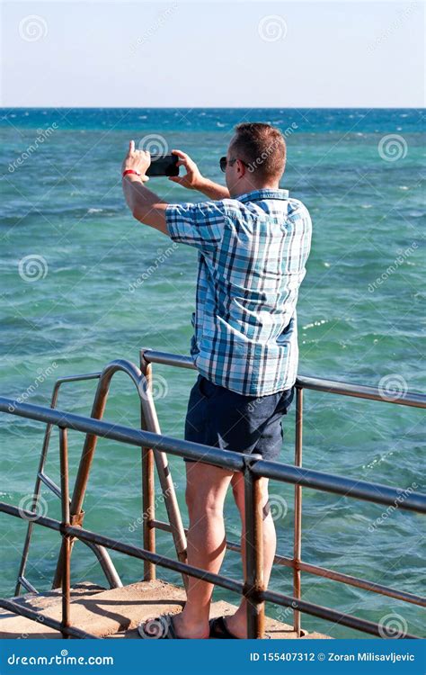Tourist And Traveler On Beach Pier Is Taking Pictures Using Camera His