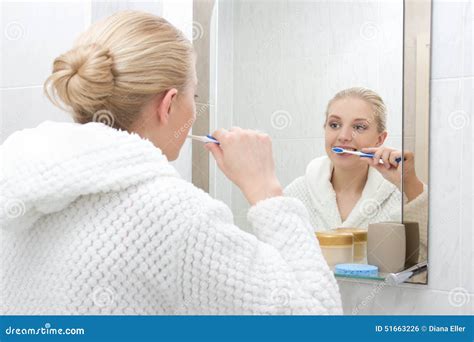 Beautiful Woman Brushing Teeth And Looking At Mirror In Bathroom Stock