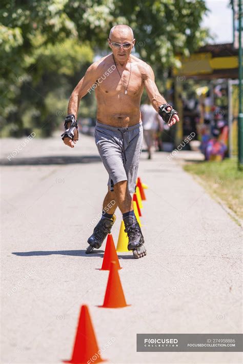 Shirtless Senior Man Rollerskating In Park On Road With Cones Happy