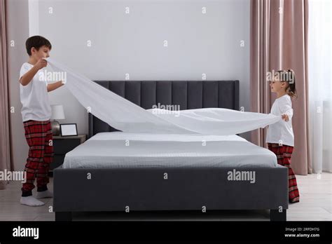 Brother And Sister Changing Bed Linens Together In Bedroom Stock Photo