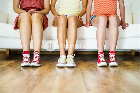 Three Young Girls Sitting On Sofa Closup On Legs And Sneakers Royalty