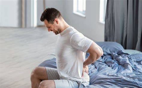 Man Massaging Aching Back Sitting In Bed At Home Stock Image Image Of