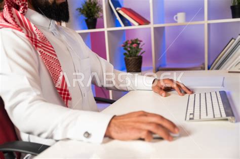 صورة مقربة لرجل اعمال سعودي خليجي يعمل في مقر الشركة ، يستخدم جهاز تقني لانجاز مهامه ، يرتدي