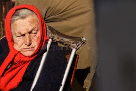 Defocus Ukrainian Elderly Woman In Red Shawl With Crutches Sitting