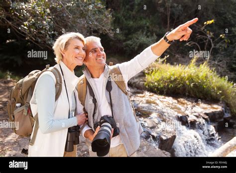 Cheerful Senior Couple Hikers Pointing In Mountain Valley Stock Photo