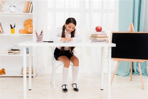 Free Photo Cute Schoolgirl Sitting At Desk And Exercising In Classroom
