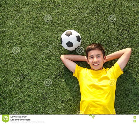 Happy Teenage Boy With A Soccer Ball Lying On The Green Lawn Stock