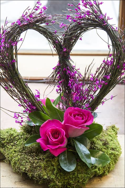 A Heart Shaped Arrangement With Pink Roses And Greenery On A Mossy
