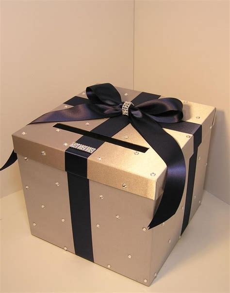 A Silver And Black Gift Box With A Bow On It S Side Sitting On A White