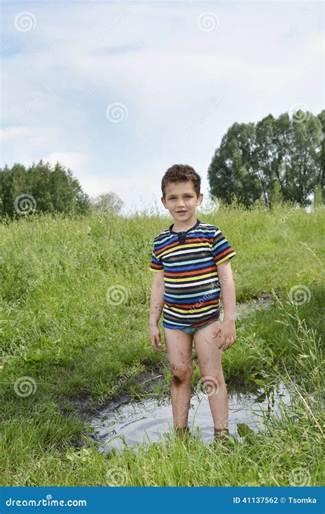 Dirty Rural Boy Stands Barefoot In A Puddle Stock Photography