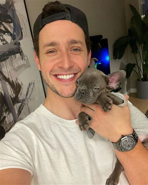 A Man Holding A Puppy In His Right Hand And Smiling At The Camera While